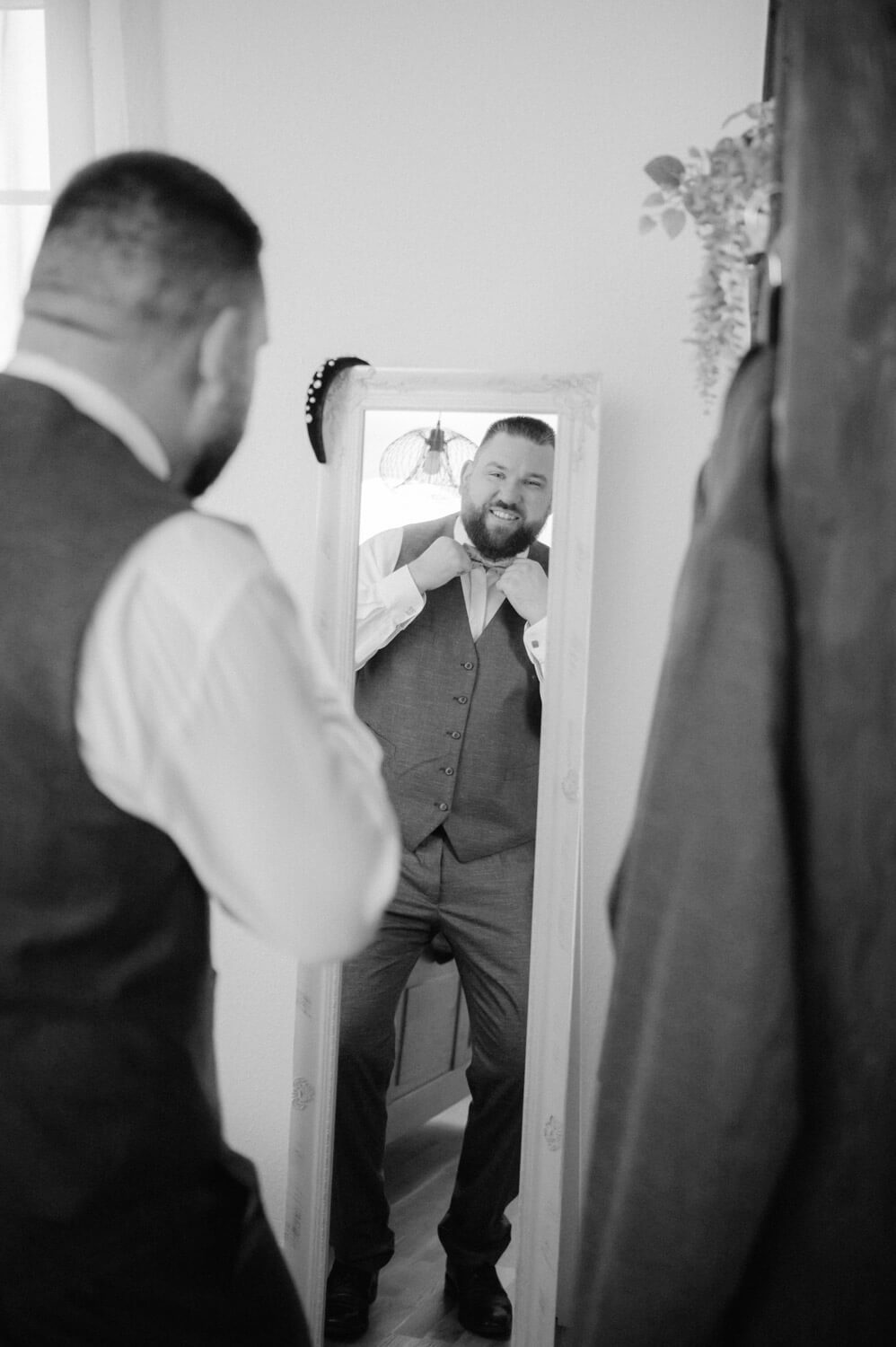 Bräutigam richtet seine Fliege vor dem Spiegel beim Getting Ready