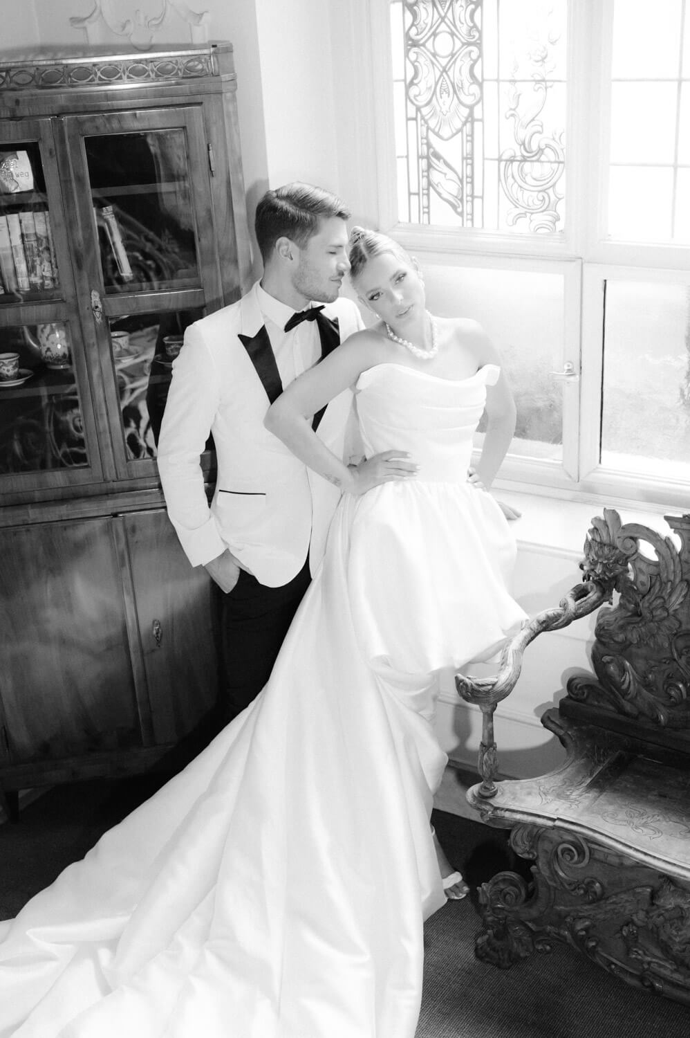 Brautpaar lehnt elegant am Fenster in einer schwarzweissen Hochzeitsaufnahme