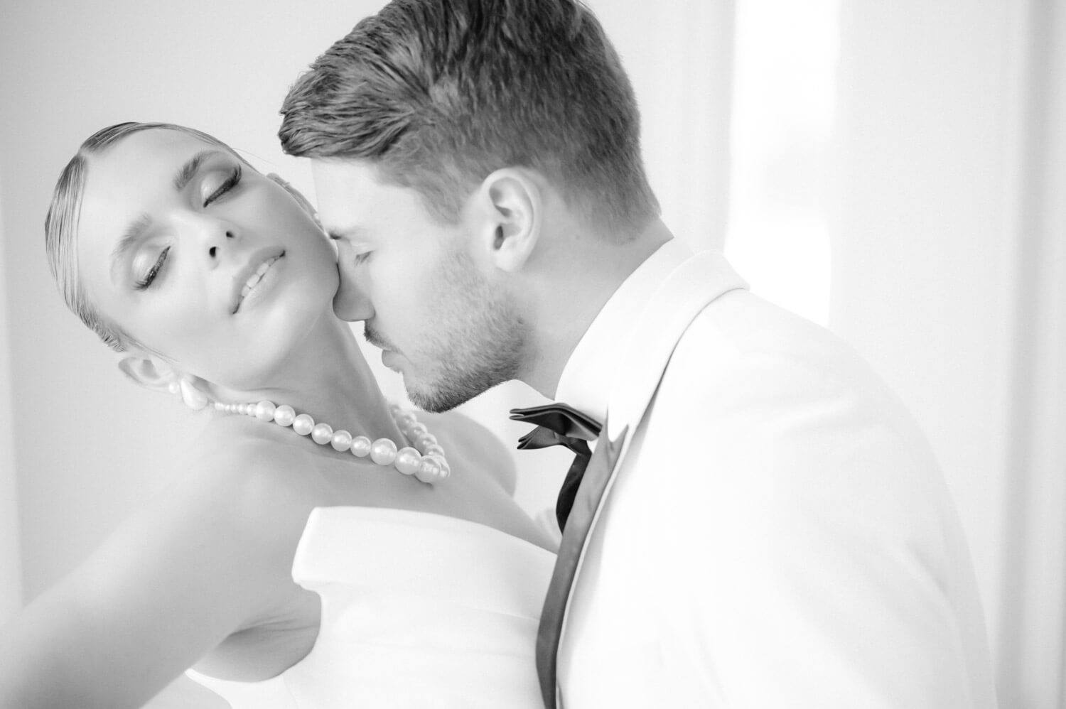 Schwarzweissaufnahme eines Bräutigams, der die Braut sanft am Hals küsst.