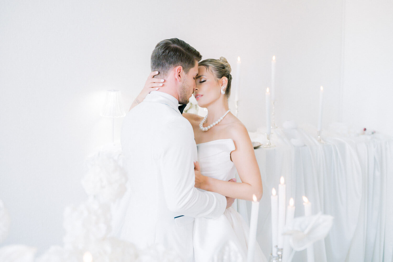 Braut und Bräutigam stehen eng umschlungen in einem hellen Raum mit brennenden Kerzen.