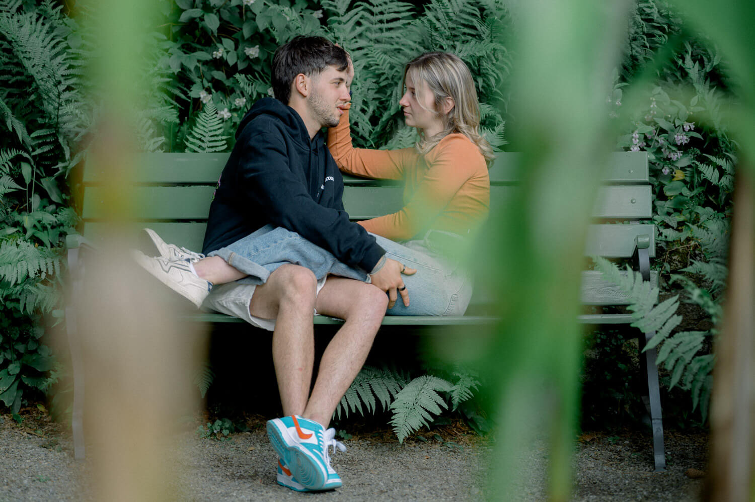 Paar sitzt eng beieinander auf einer Bank im Grünen während eines natürlichen Verlobungsshootings