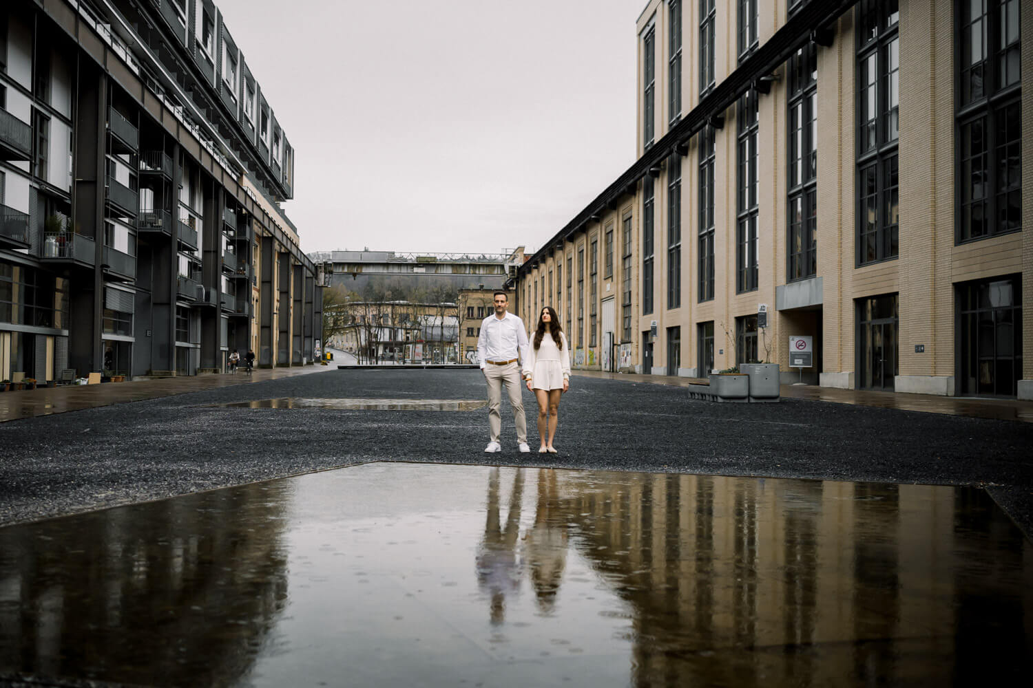 Paar steht vor moderner Industriearchitektur mit Spiegelung in einer Pfütze in Winterthur