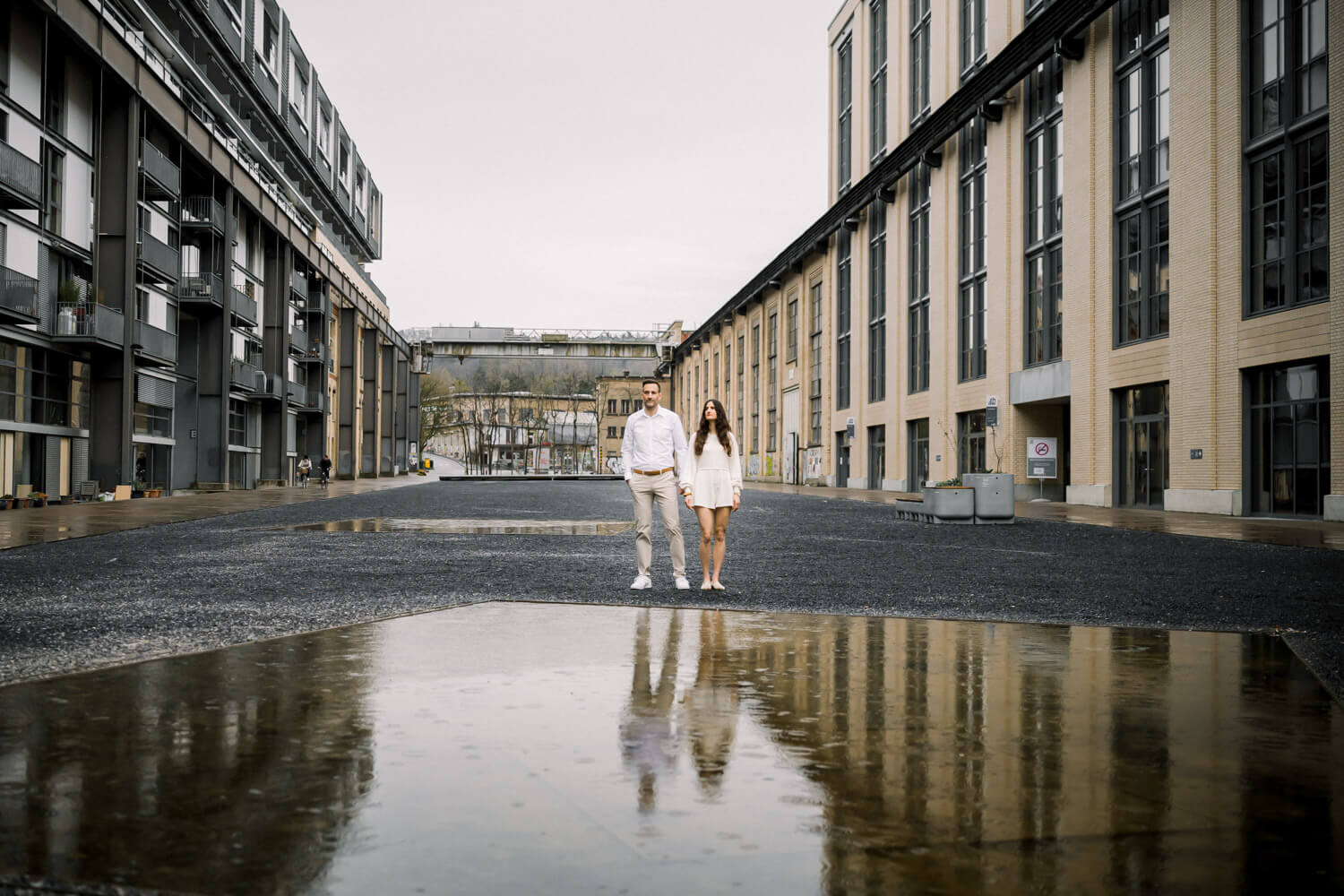 Paar steht vor moderner Industriearchitektur mit Spiegelung in einer Pfütze in Winterthur
