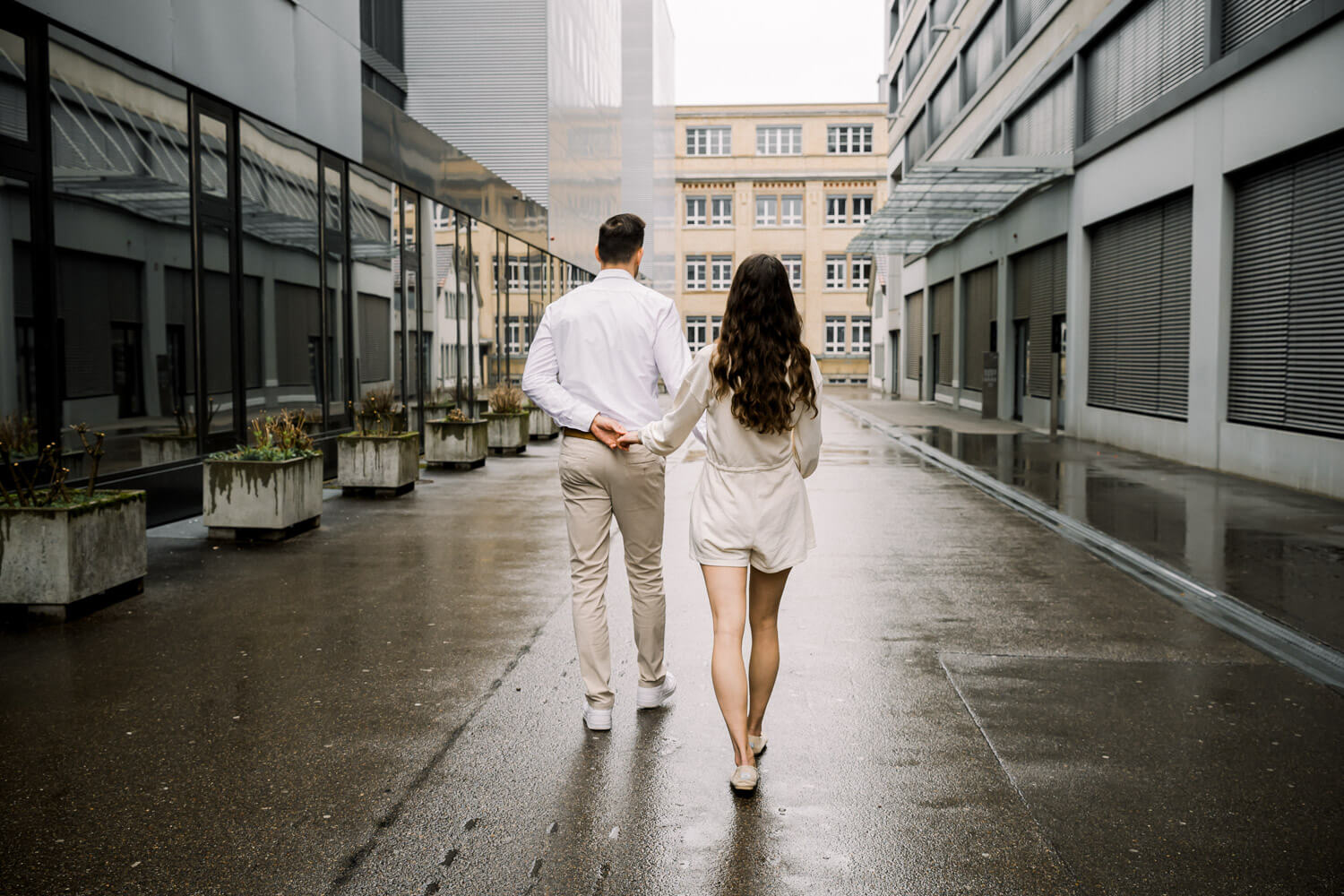 Paar geht von hinten durch eine moderne urbane Strasse mit nassem Boden