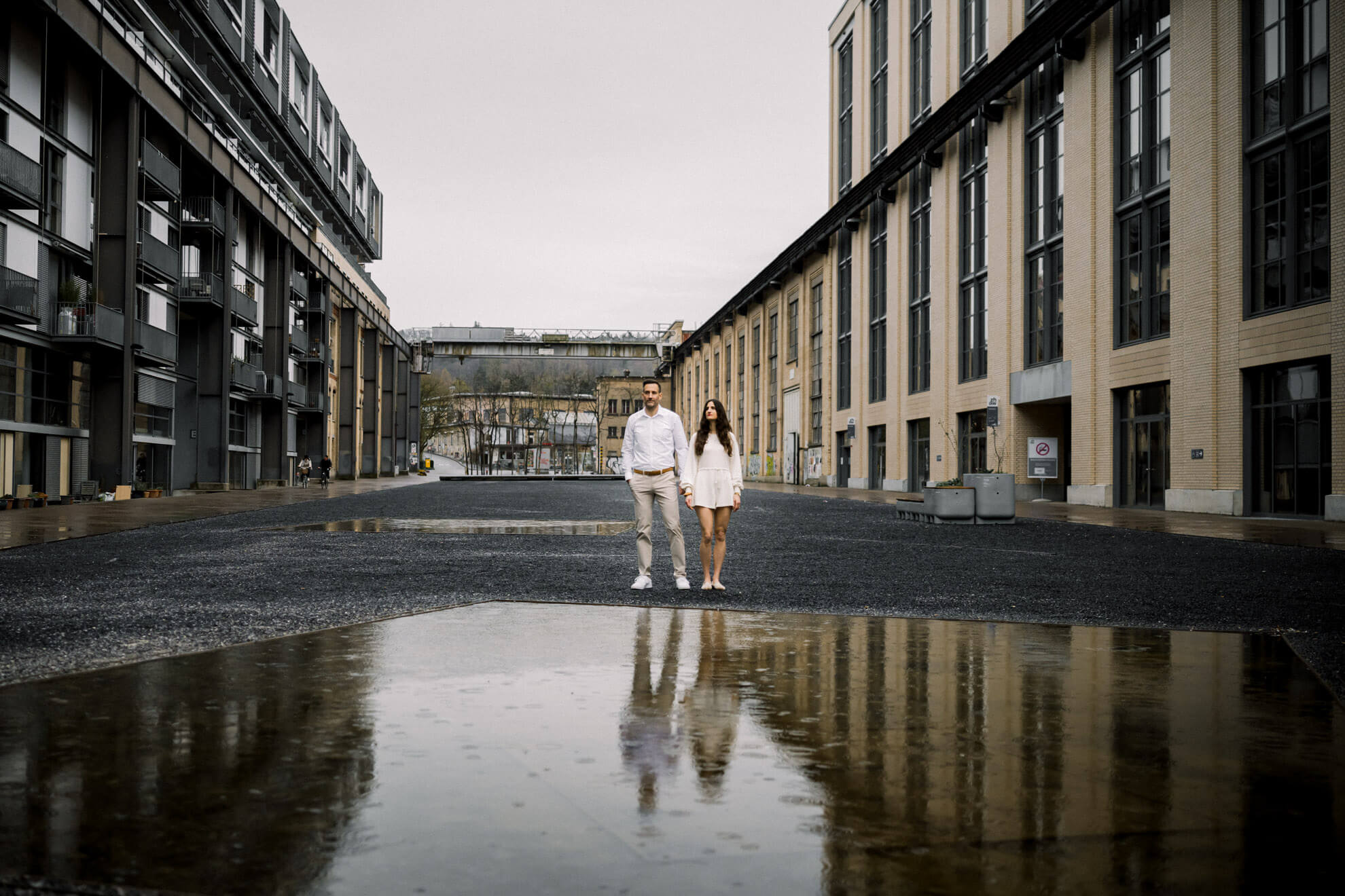 Verlobungsshooting in Winterthur mit Paar vor moderner Industriearchitektur und Spiegelung in einer Pfütze